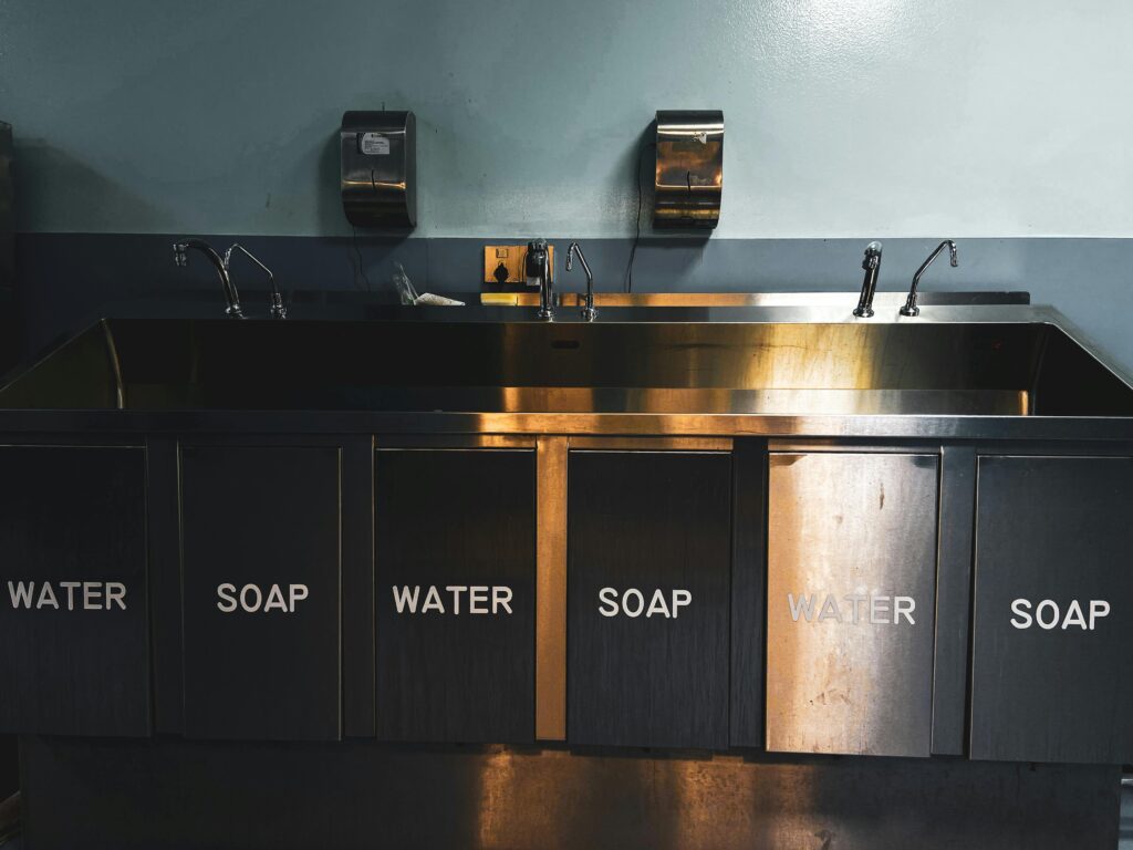 pexels-photo-10949030-10949030 A stainless steel industrial kitchen sink with labeled compartments for water and soap.