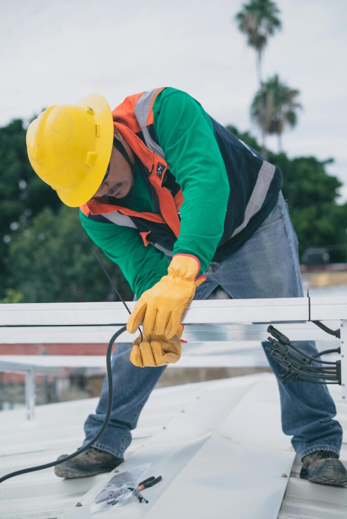 pexels-photo-8853472-8853472 A construction worker wearing PPE installs electrical equipment on a roof.