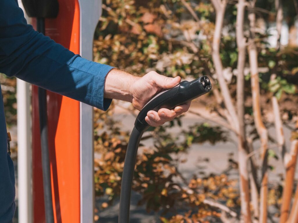 pexels-photo-9799732-9799732 Hand holding an electric vehicle charger at a station outdoors with autumn trees.