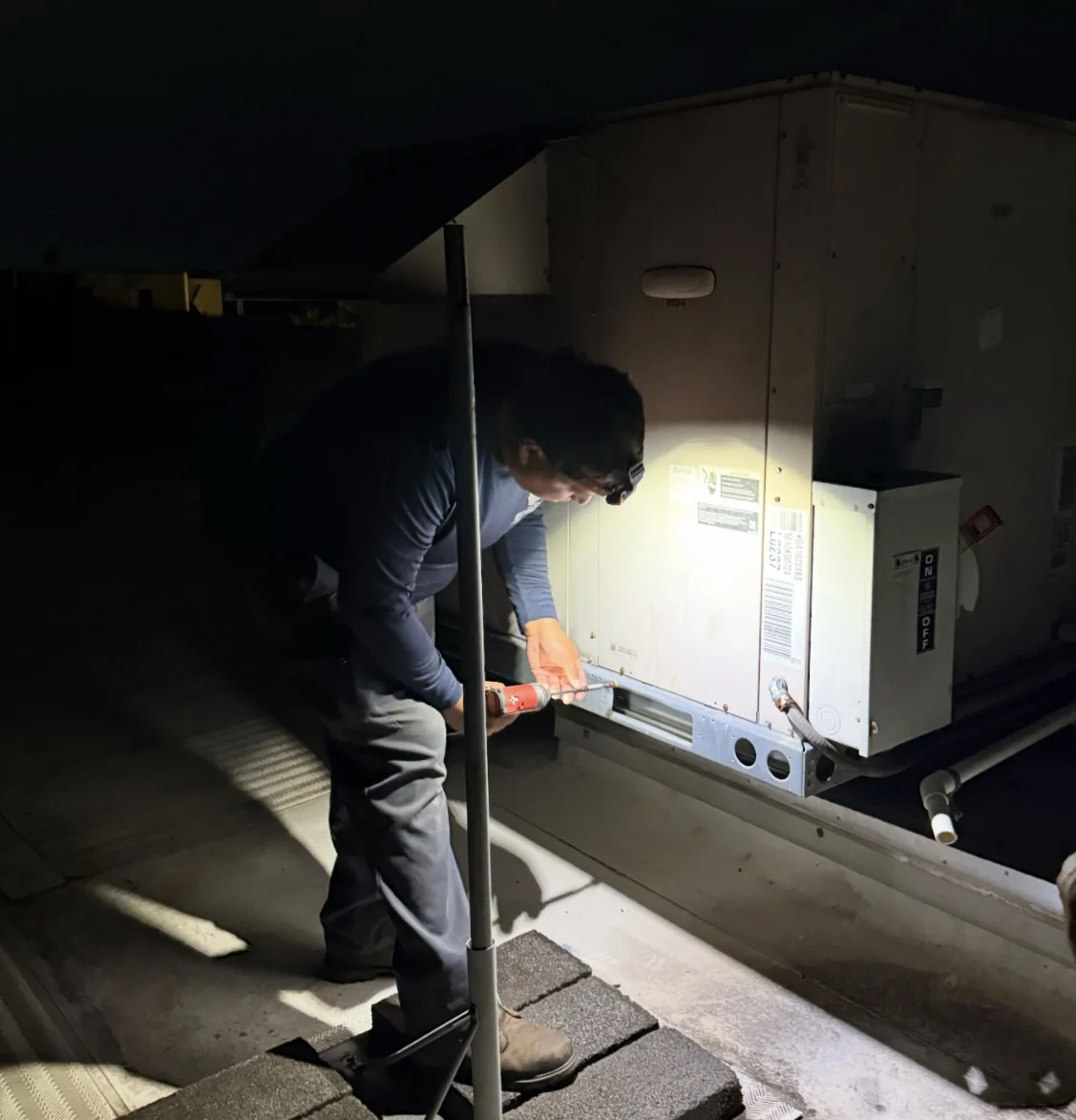 Eco-One technician servicing a rooftop HVAC unit after dark
