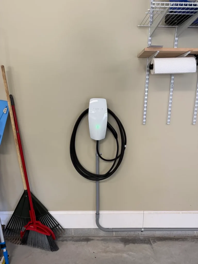 Tesla Wall Connector with coiled charging cable and surface-mounted conduit on a garage wall
