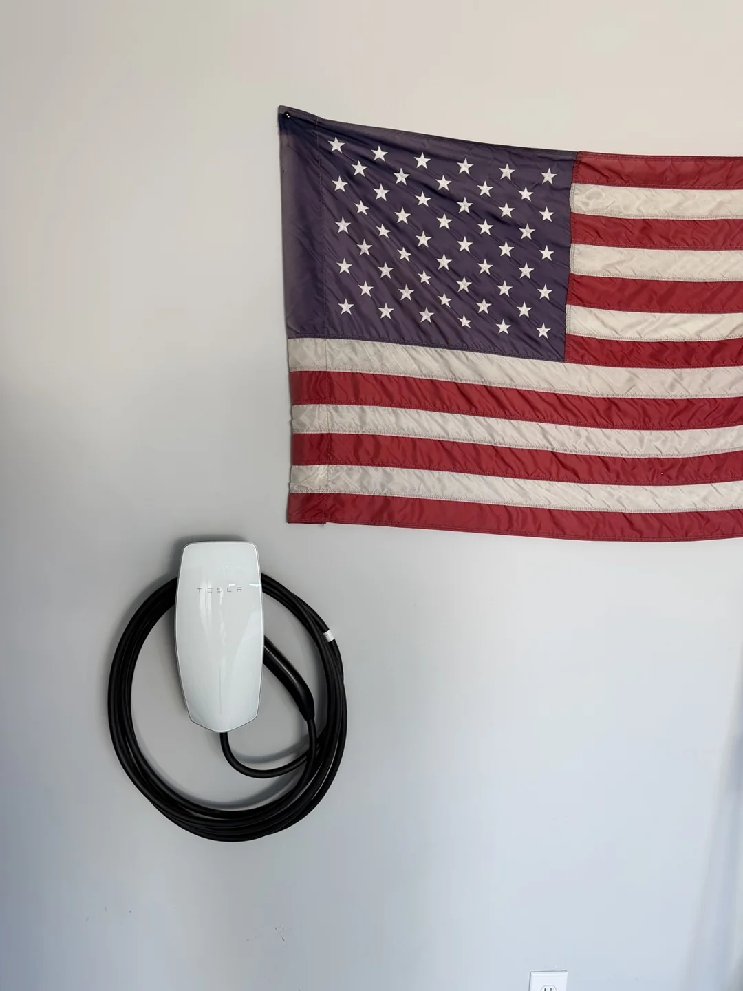 Tesla Wall Connector and charging cable installed on a garage wall beneath an American flag